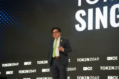 A man wearing glasses and a dark jacket speaking on stage at the TOKEN2049 Singapore event.