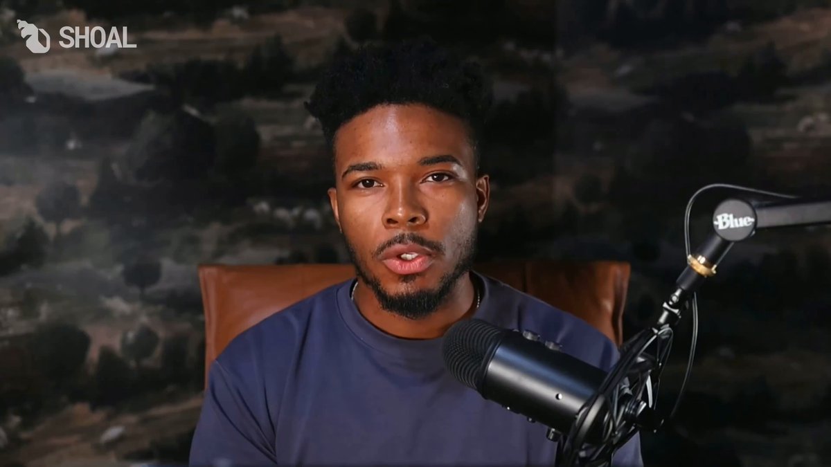 The image features a man wearing a blue shirt sitting behind a microphone, likely participating in an online podcast or live stream. The background of the image has a dark color, which contrasts with the man's attire. There are two microphones visible in the scene - one being held by the man and another placed on top of his head. The image also contains text that reads "GPU-Backed Debt and the case for the End of SaaS Credit Shoal Signal Ep. 7 with @0xZergs co-founder/CEO of @USDai_Official hosted by @zaddycoin AI compute is being built faster than the financial system can finance it." This text seems to be related to the content of the image, possibly discussing the current state of technology or the impact of the ongoing pandemic on various aspects of life.