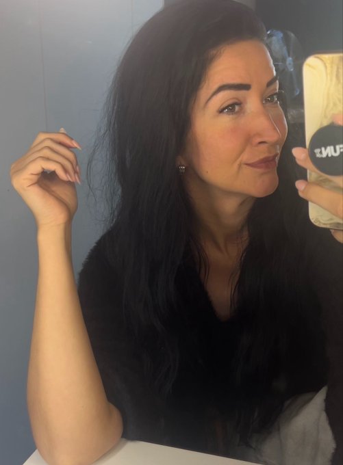 A woman with long dark hair takes a selfie in a mirror, holding a gold phone with a "FUNK" sticker. The image accompanies a cheerful Monday morning greeting to her XRP crypto community, sharing an upbeat, motivational message to start the week.