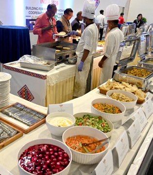A "BRICS SUMMIT 2026" event features a catering setup by ITC Hotels, where chefs in white uniforms serve world leaders from a buffet line offering colorful dishes including beet salad, pasta, and garnished potatoes. The image highlights the upscale dining arrangement for the international summit held in New Delhi, India.