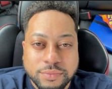 A selfie of a man with a short beard sitting in a car, with a blue jersey featuring 'MESSI 10' partially visible in the background.