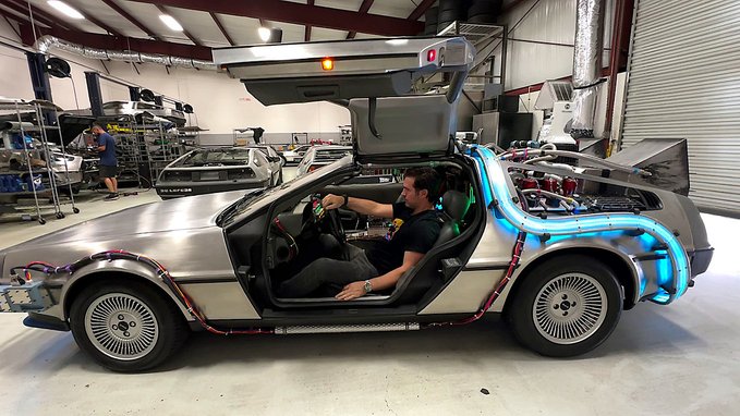 A man sits inside a DeLorean DMC-12 in a garage, with the gull-wing door open and blue accent lighting illuminating the vehicle, likely as part of a workshop or restoration scene.

The accompanying string (DmcqxT7WXgXhq2LHURQ2h8GA5PeCBuMTLeyaj6MXhf3p) appears to be a Solana wallet address or transaction signature, with no direct visual relation to the image beyond sharing "DMC" as a possible thematic link to the DeLorean DMC-12 model.