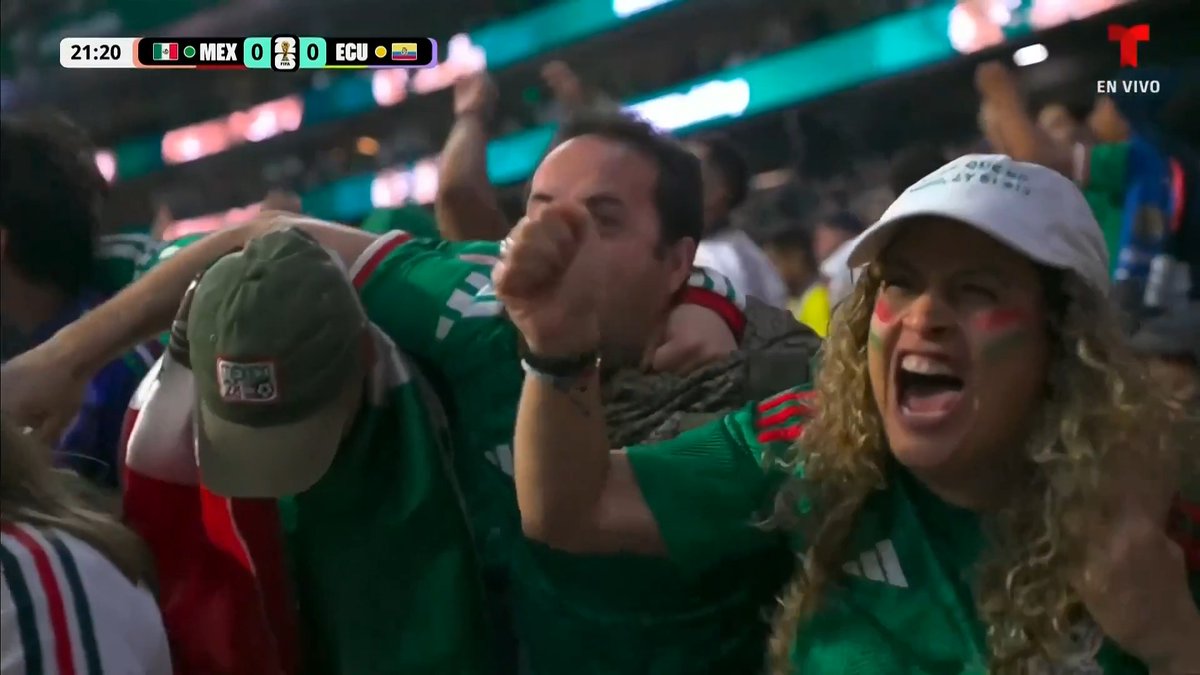 Mexican football fans in green jerseys cheering at a stadium, with a scoreboard showing Mexico vs Ecuador tied 0-0 at 21:20, broadcast on Telemundo 'EN VIVO'.