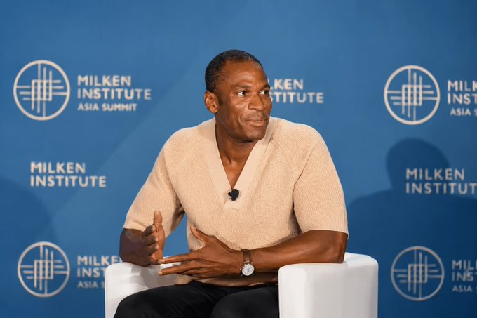 A man speaks on stage at the Milken Institute Asia Summit, gesturing with his hands while seated, with the event's logo and branding visible on the blue backdrop behind him. The image appears to be from a panel discussion at the summit, but there is no direct visual connection to the BitMEX shutdown announcement mentioned in the accompanying post.