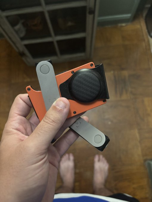 A hand holding a small orange and black gadget with extending metal arms.
