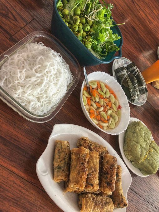 A table spread of Vietnamese food featuring rice noodles, fried spring rolls, fresh herbs, bean salad, and green dipping sauce.