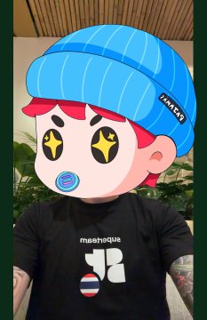 A digitally edited image shows a cartoon-style character with a blue beanie, star-shaped eyes, and a pacifier superimposed over a person wearing a black "mashoiqua" t-shirt.