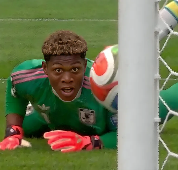 A goalkeeper in a green jersey with pink gloves dives desperately toward the goalpost, eyes wide as he watches the ball narrowly miss the net, mirroring the tense, close-call feeling of watching a volatile trading chart tick against your position.