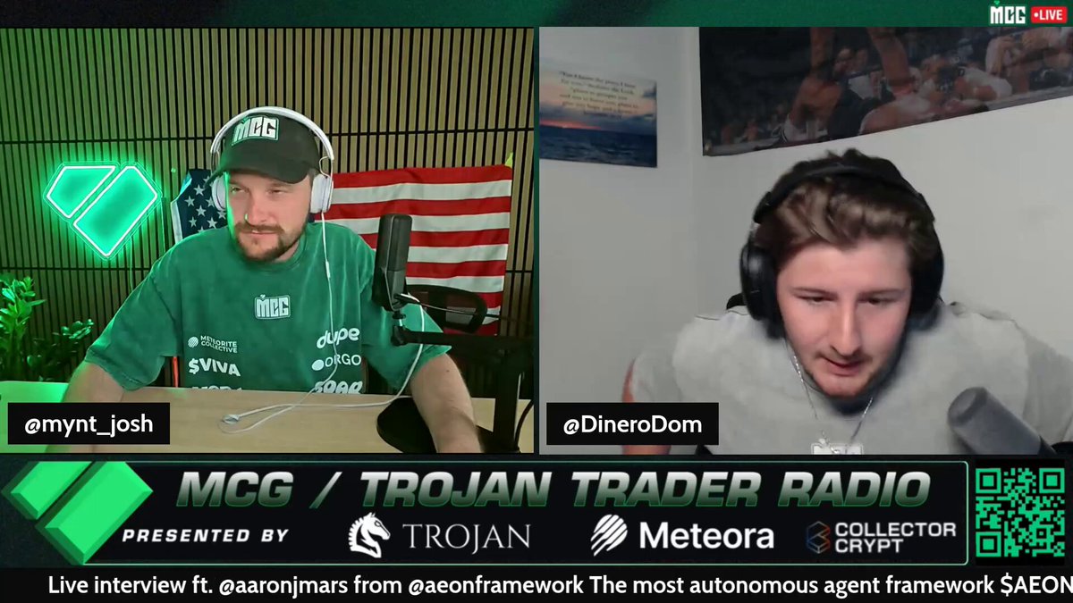The image shows two men talking into microphones during an event on MCG called "Troy Trader Radio". One man appears to be wearing a green shirt while the other person wears a grey one. They are sitting behind a table with microphones, indicating that they might be discussing a topic related to investing in cryptocurrency or cryptocurrency mining. The image also contains text elements such as @0xgilbert and #usepodai which might provide additional context about this event on MCG.