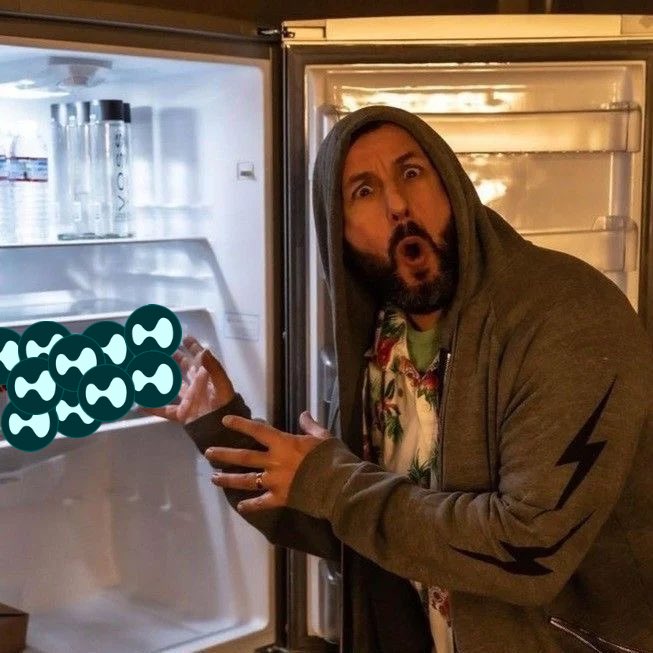 A man in a green hoodie looks in shock into an empty refrigerator while holding a cluster of green Kusama (KSM) crypto logos.