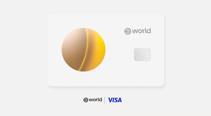 The image features a white credit card, which appears to be from World Bank or another organization. It has a gold circle design on its front, and the text "World" and "Visa" are visible. The background of the image is gray, providing a neutral backdrop that allows the colors of the credit card to stand out.