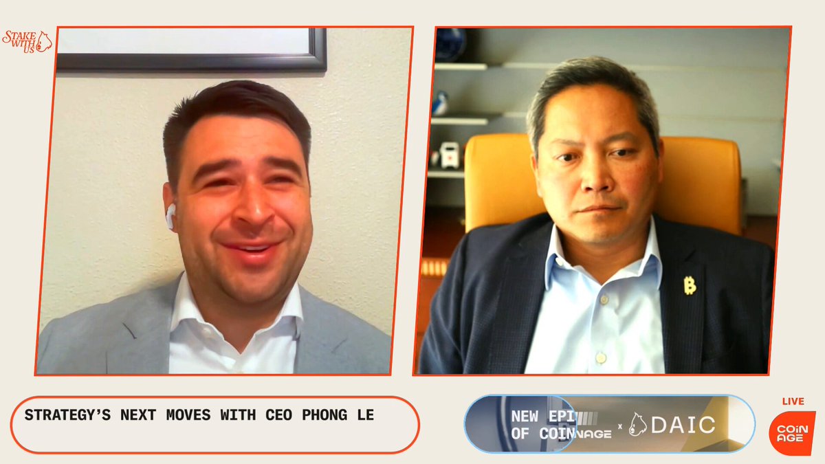 The image shows two men sitting behind a desk, with one man wearing a suit and the other wearing a blue shirt. The background of the image features a gray wall, which has a picture hanging above it. There are also some text elements on the image that read "I asked Strategy CEO Phong Le about @saylor using AI to spin up $STRC from taking three years to probably taking 8 months."