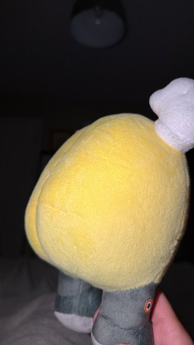 A close-up photo of a yellow plush toy's rear end being held by a hand, featuring white fluffy tail-like material and gray fabric legs.