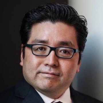 A professional headshot of a man with dark hair, wearing rectangular black-framed glasses and a dark suit with a tie, shown against a plain gray background. The image accompanies news that Tom Lee's BitMine has purchased 12,535 ETH valued at $30 million.