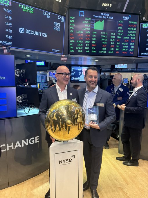 Two men stand in front of the New York Stock Exchange ticker screens, holding a large golden sphere, likely celebrating the tokenization of over $300M of SECZ on Avalanche. The ticker screens in the background show stock information and the NYSE logo.