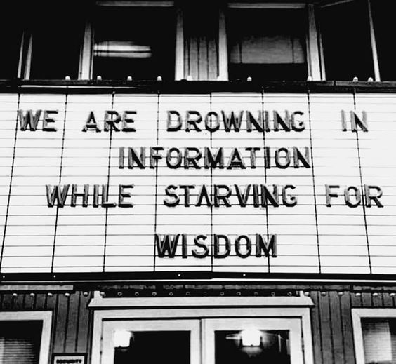A black-and-white photograph shows a theater marquee displaying the quote "WE ARE DROWNING IN INFORMATION WHILE STARVING FOR WISDOM" above the building's entrance.