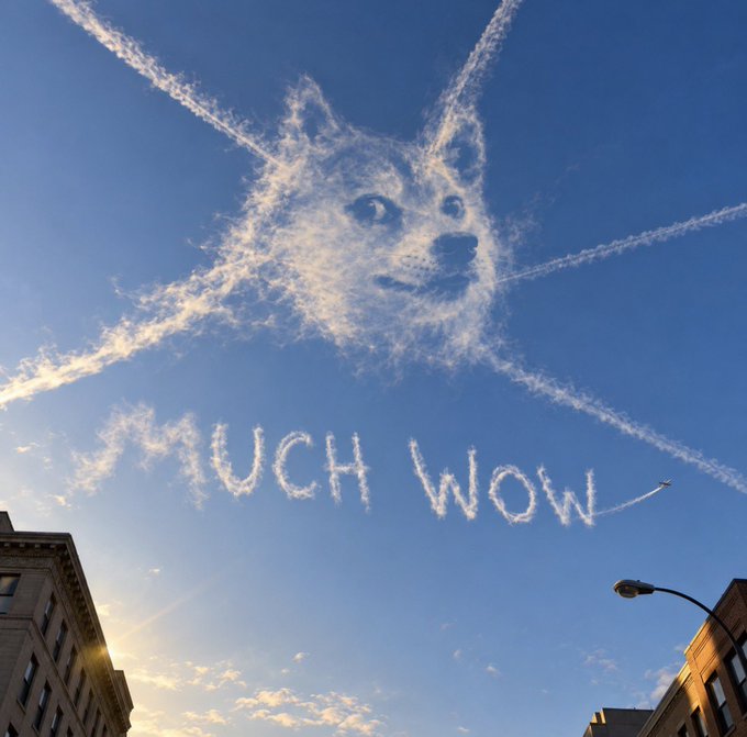 A creative sky art image shows a Doge face and the text 'MUCH WOW' formed by clouds and contrails in a blue sky above city buildings.