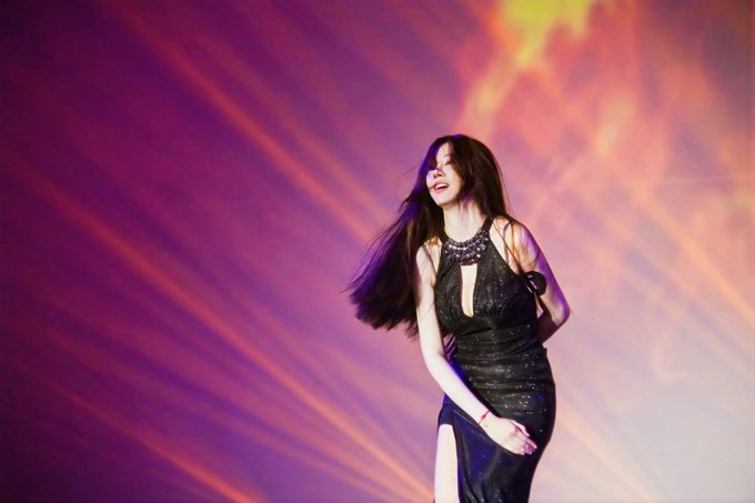 The image features a woman wearing a black dress with long hair standing on stage. She appears to be singing or performing, possibly at a concert. The background of the photo has purple lights shining down on her, creating an interesting visual effect. The caption reads "I was honored to finish as the 2nd runner-up in the past season of Miss HTX." This suggests that she is participating in a MissHTX competition and has achieved a significant accomplishment within it.