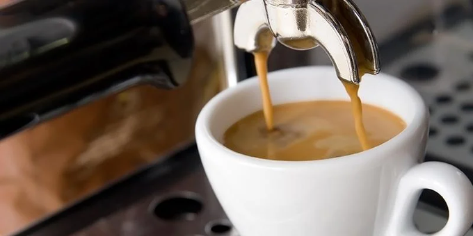 A close-up shot of an espresso machine pulling a double shot of coffee into a small white ceramic cup.