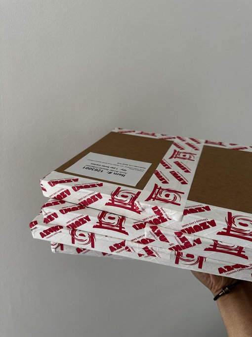 A hand holds a stack of pizza boxes branded with the Azuki logo and "ARBITS" text, with a label reading "Item #: 1750201," fitting perfectly with the "Azuki pizza friday" theme.
