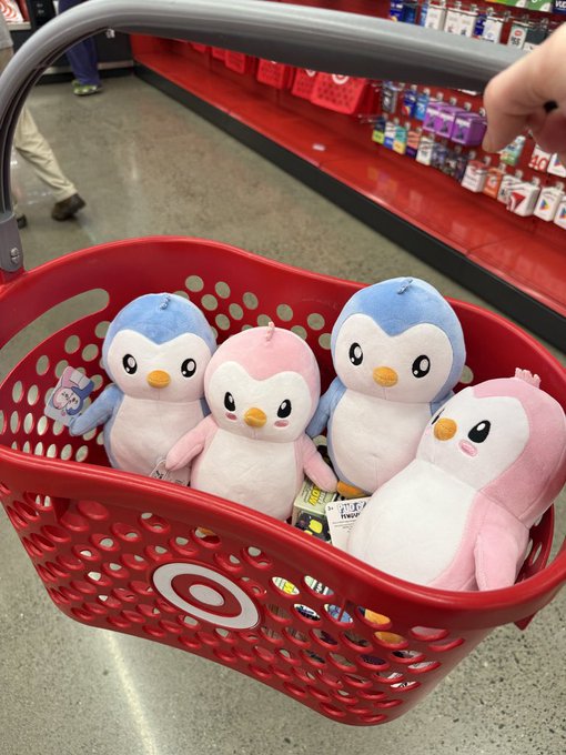 A red Target shopping basket filled with four plush penguins in blue and pink colors, being held in a store aisle.