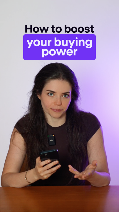 A woman with long dark hair sits at a wooden table holding a smartphone, looking directly at the camera, with bold text overlay reading "How to boost your buying power" — visually introducing the concept of increasing capital without liquidating existing crypto holdings, as referenced in the post about buying more Bitcoin without selling current crypto.