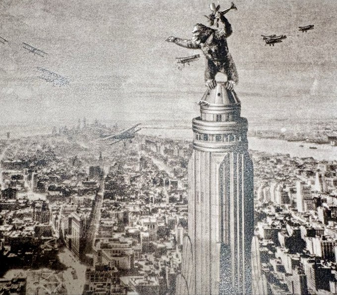 A black and white illustration depicting King Kong sitting atop a skyscraper, likely the Empire State Building, while biplanes fly around him in a vintage cityscape.
