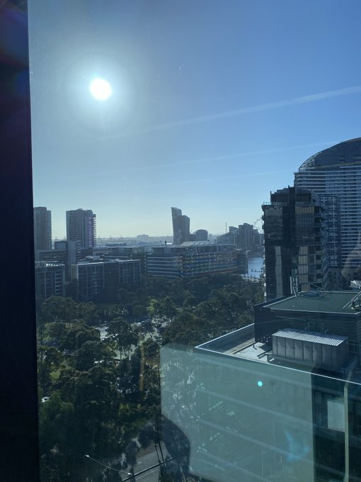 A photograph taken through a window showing a bright sunny day with a cityscape, including high-rise buildings, trees, and a body of water in the distance.