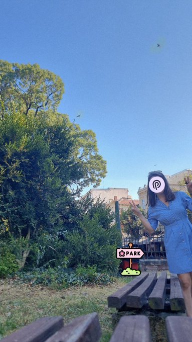 A woman makes peace signs in a sunny park next to a sign that reads "PARK," matching her relaxed vibe and the "good vibes and chill day" mentioned in her PYTH post.