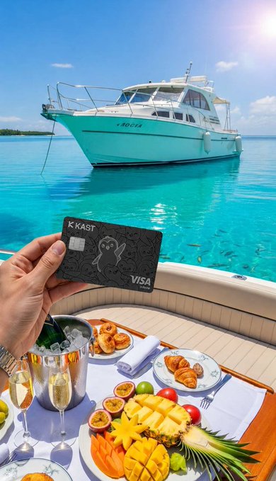 The image shows a person holding a credit card, possibly Visa or Mastercard, over a plate of food that includes fruit such as bananas, pineapples, and mangoes. The scene takes place near a boat on the water with a clear blue sky in the background. The person is standing next to a dining table filled with various dishes, including a wine glass, a bottle, and other items like bowls and spoons. The image conveys a sense of luxury and relaxation as it captures a moment where someone is enjoying their breakfast by the water while holding their credit card.