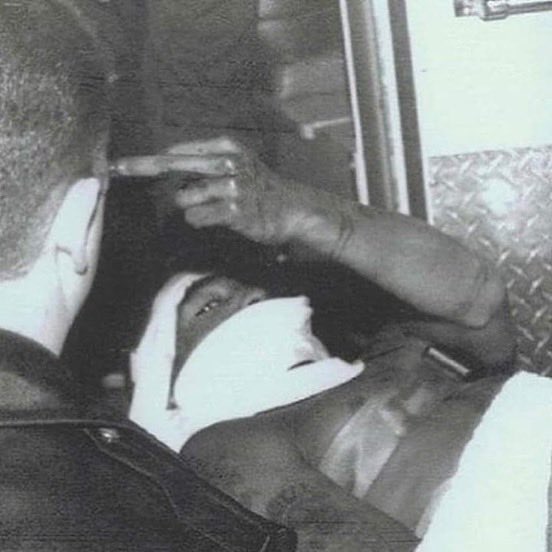 A grainy black-and-white photo showing a person lying down with their face covered and one arm raised, appearing distressed.