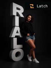 A woman in a black sweater and denim skirt stands next to large 3D letters spelling 'RIALTO' with the 'Latch' logo in the top right corner.