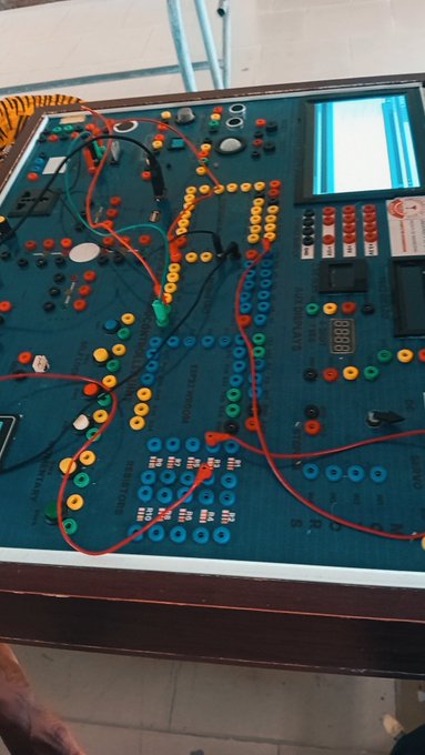 An electronic circuit trainer/educational kit board with various components, buttons, and colorful wiring connections on a green surface.