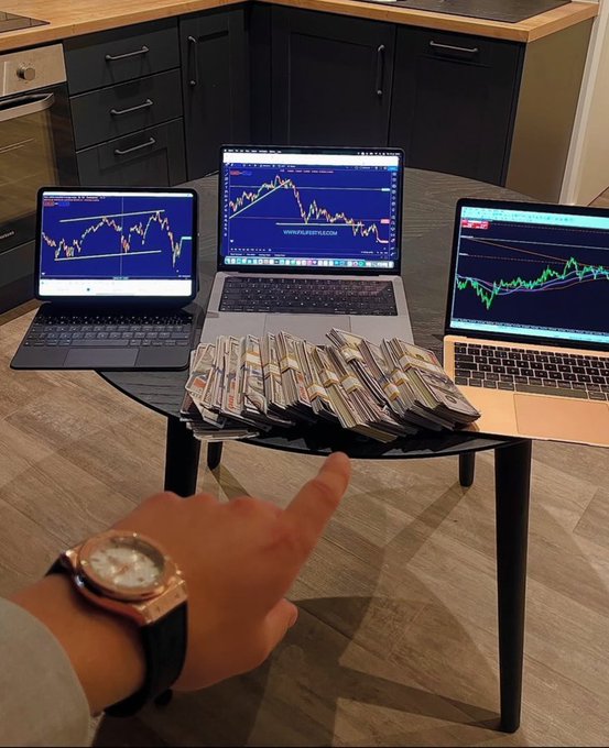 A person pointing at stacks of cash arranged on a black coffee table in front of three open laptops displaying financial trading charts (TradingView).