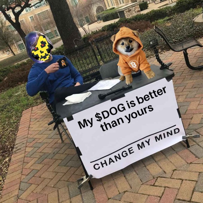 A person wearing a pixelated Doge mask sits at a table next to a Shiba Inu dog wearing a Bitcoin hoodie, with a sign reading 'My $DOG is better than yours - CHANGE MY MIND'.