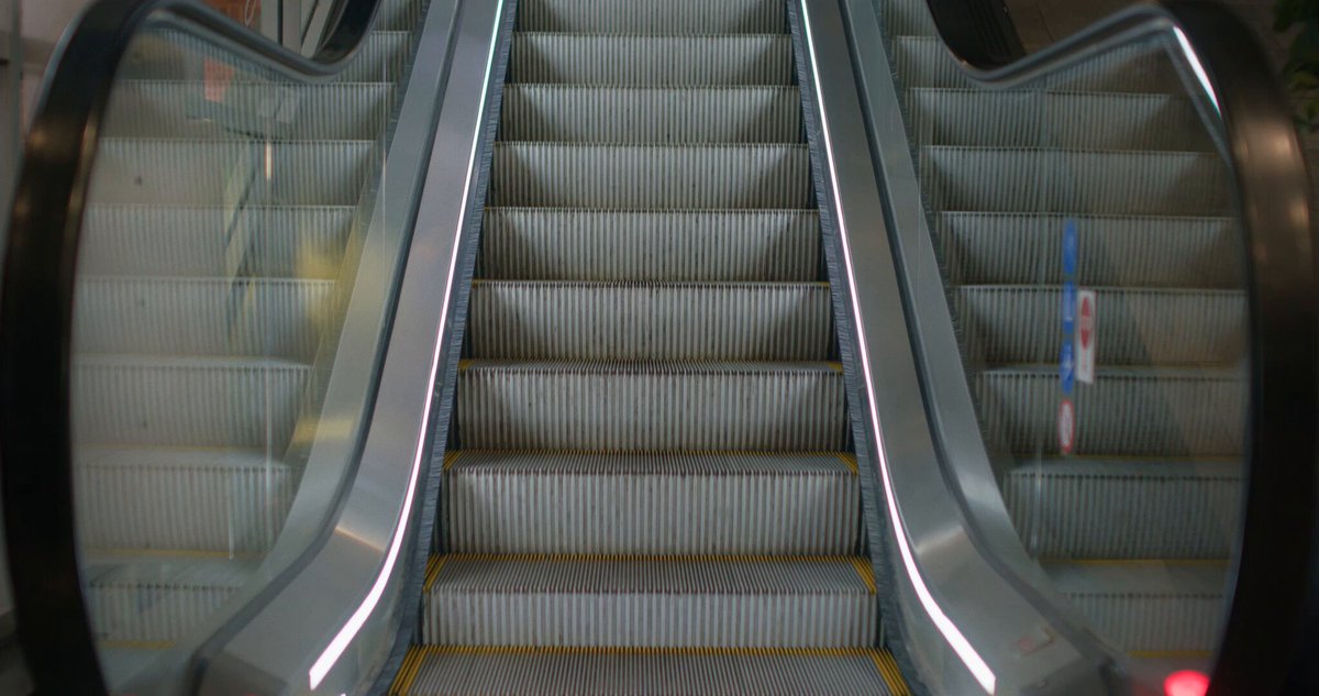 iced glass escalator with a black frame and white stripes, leading to an unseen destination.