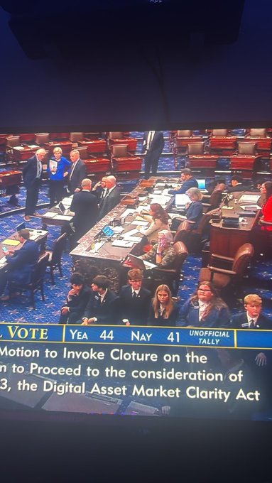 A TV screen showing the U.S. Senate floor with on-screen text reading 'YEA 44 NAY 41 UNOFFICIAL TALLY' for a vote on 'Motion to Invoke Cloture' regarding 'the Digital Asset Market Clarity Act'.