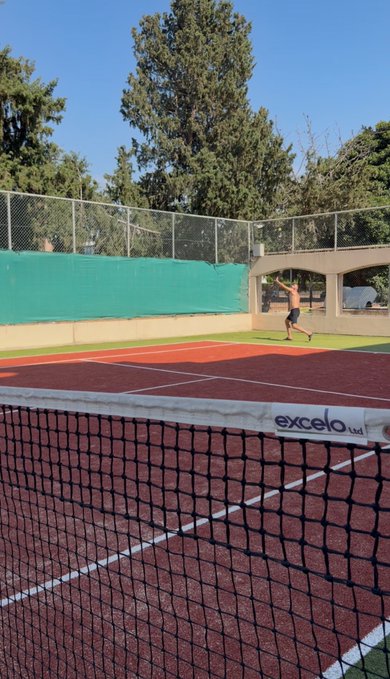 A shirtless man practices tennis on a sunny outdoor court, with the "excelo" branded net in the foreground suggesting a casual weekend warmup to match the "Gm friends" greeting.