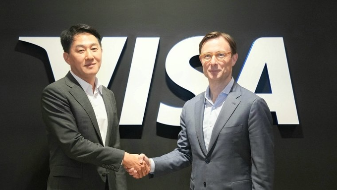 Two men in business attire shaking hands in front of a large white 'VISA' logo on a black background.