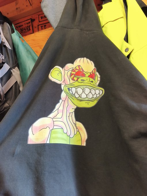 A black hoodie displays a colorful, cartoonish graphic of a grinning, lanky creature with green skin and a red bow on its head.