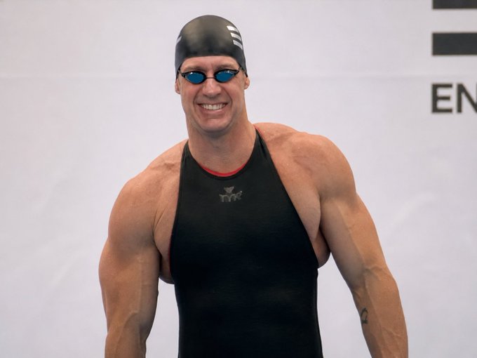 The image features a muscular man wearing a black swimsuit, standing against a white background with his arms crossed over his chest. He has sunglasses on and appears to be smiling for the camera. The caption reads "i can stay in stealth longer than you can fud", which is likely a reference to the character from the movie "The Dark Knight". This reference adds an interesting element to the image, as it connects the man's physical appearance with a popular film franchise.

In addition to the main subject, there are two other people visible in the background, but they do not appear to be the focus of the image. The overall composition and content suggest that this photo might have been taken at an event or gathering related to "The Dark Knight" or another superhero-themed movie.