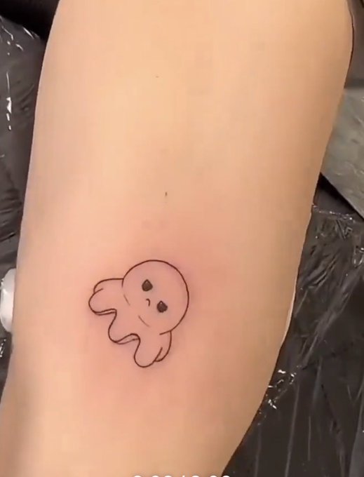 Close-up of a small, minimalist black ink tattoo of a cute cartoon character on a person's arm.