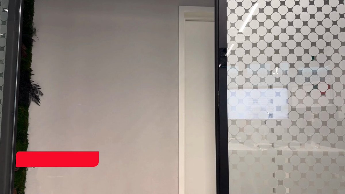 The image features a white door with a glass window, which has a red mark or label on it. The door appears to be closed, but there's an interesting detail about the wall behind it. The wall is covered in small circles, creating a unique pattern that adds visual interest to the scene.