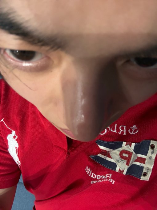 A close-up, angled shot of a person's face looking down at the camera, wearing a red polo shirt with a "Reebok" logo and an emblem featuring the number "9" with nautical anchor designs and "1998" text. The casual selfie style aligns with the post's hashtag #LEO/#리오 and personal branding reference.