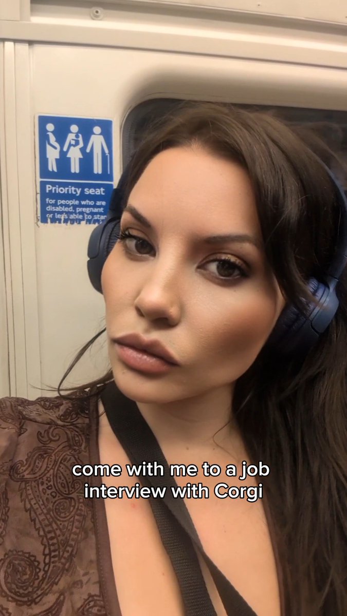 A selfie of a woman wearing headphones on public transit, with the caption 'come with me to a job interview with Corgi' visible over a priority seat sign.