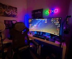 A dimly lit gaming/streaming setup featuring an ultrawide monitor with a PlayStation, neon lighting, a gaming chair, and an illuminated 'PS5' neon sign on the wall.
