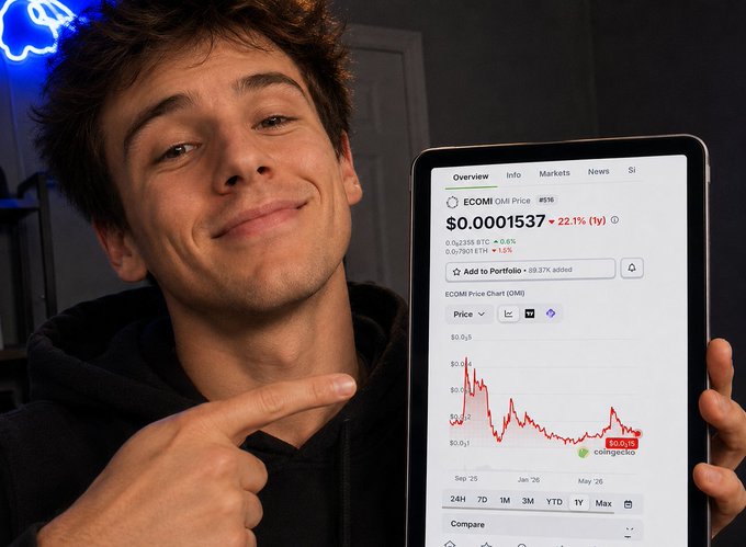 A young man in a black hoodie smiling and pointing at a tablet screen displaying ECOMI (OMI) price information, showing a value of $0.0001537 with a 22.11% increase.