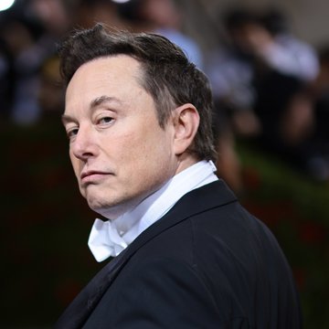 The image features a man dressed in a suit with a white shirt and a tie, standing against a blurred background of people. The caption reads "Elon Musk' s wealth has surpassed the total market value of Bitcoin - 1,300,000,000,000 dollars". This statement is related to the image as it suggests that the man's wealth could potentially be greater than the current value of Bitcoin.