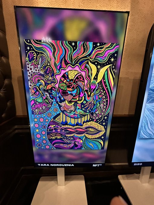 A vibrant, psychedelic digital artwork labeled 'TARA NOROUZIA NFT' is displayed on a lit screen in what appears to be a gallery or exhibition space.
