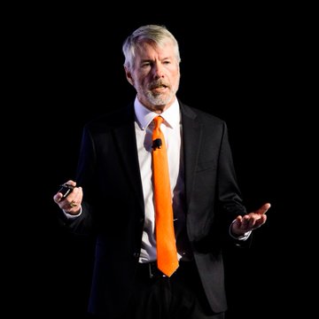 The image features an older man wearing a suit and tie with an orange tie, standing against a black background. The caption reads "LATEST: Michael Saylor: Would you rather have Strategy buy 200,000 Bitcoin a year and sell 10,000, or buy no Bitcoin and sell no Bitcoin?". This post is related to the image because it features a man wearing a suit and tie giving a speech, which could be interpreted as an advertisement for a company like Strategy.